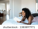 Attractive black woman lying down on bed reading a book at home