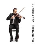 Small photo of Full length portrait of an elegant young man sitting and playing a violin isolated on white background