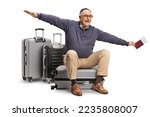 Mature man sitting on a suitcase and gesturing flying isolated on white background