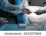 Small photo of Cropped side view of unrecognizable nurse assists surgeons, giving surgical clamp with tampon during surgical operation. Doctors team working performing surgery in intensive care unit