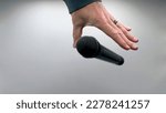 Small photo of Caucasian Man Dropping the Mic Sequence - Popular Performance All Black Dynamic Microphone - Hands Only - White Background - Simple Concept