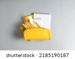 Small photo of Back to school concept. Yellow school pencil case with filling school stationery, notebook, pens, pencils. Yellow school accessories on grey background. Flat lay, top view, copy space