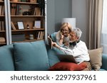 Small photo of Simple living. Happy middle-aged senior couple 70s husband and wife sit relax on couch in living room reading book drinking tea together, calm elderly 60s couple booklovers rest at home enjoy life