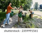 Small photo of Group of young conscious activists collect and clean up trash from the park to keep the environment clean. Friends reduce pollution of green areas in the city after irresponsible and arrogant citizens