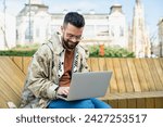 Small photo of Young hipster millennial man world traveler nomadic living lifestyle sitting outdoor using laptop computer to search for new travel destination and place to visit. Generation Z expatriate male concept
