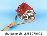 Small photo of Plastic model of a house in a hangman's noose on a blue background. The house is trapped. It is difficult to pay for buying a house on credit.