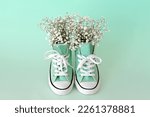 Small photo of Beautiful casual shoes with flowers inside light background. Flowers in sneakers. Walk. Modern unisex footwear, sneakers. Fashionable stylish sports casual shoes. High quality photo
