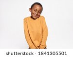 Horizontal shot of cute handsome dark skinned little boy shrugging shoulders feeling embarrassed with uncomfortable question, looking down with shy timid smile. Human emotions and body language