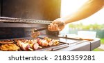 Small photo of A young man hand is grilling some meat and vegetable skewers on a huge gas grill, food concept
