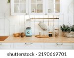 Small photo of Wooden worktop filled with kitchen accessories in a bright Scandinavian kitchen interior with cabinets and shelves. Modern white kitchen