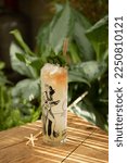 Small photo of Zombie Tiki Cocktail in tropical glass with wooden swizzle stick and plants background