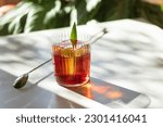 Small photo of Tropical Negroni Cocktail twist with pineapple and clear ice on a white table with shadows and a barspoon
