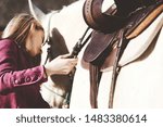 Small photo of Western lifestyle shows woman cinching up saddle for horseback ride.