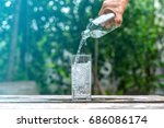 Drink water pouring in to glass over sunlight and natural green background.Select focus blurred background.
