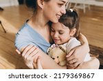 Small photo of Horizontal picture of mom and daughter cuddling on floor in living room, girl hugging favorite plush toy, after returning home from kindergarten. Conscious parenting. Happy childhood