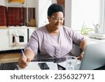 Small photo of Portrait of african american female making list of purchases checking special offers and sales online, using laptop, scrolling web-page, comparing prices, looking at screen with happy cheerful face