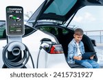 Small photo of Little boy sitting on car trunk, using tablet while recharging eco-friendly car from EV charging station. EV car road trip travel as alternative vehicle using sustainable energy concept. Perpetual