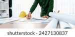 Small photo of A portrait of professional male engineer shows mistake point in blueprint on messy table with architectural plan and yellow helmet placed at modern office. Closeup. Focus on hand. Delineation.
