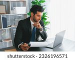 Small photo of Modern professional businessman at modern office desk using laptop to work and write notes. Diligent office worker working on computer notebook in his office work space. fervent