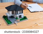 Small photo of House model is displayed on wooden meeting table with in the blurred background of real estate agent and client discuss terms and conditions of house loan or rental lease contract. Entity
