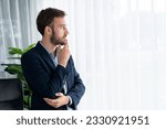 Small photo of Handsome businessman in black suit stand confidently in his modern office portrait, deep in thought about business with pensive gazing expression, thinking strategically about his next move. Entity