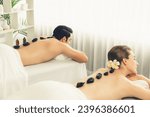 Small photo of Hot stone massage at spa salon in luxury resort with day light serenity ambient, blissful couple customer enjoying spa basalt stone massage glide over body with soothing warmth. Quiescent
