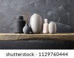 Home decor - various neutral colored vases with wood sticks on rough distressed wooden shelf against grey wall.