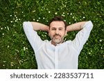 Handsome adult man lying down on grass with daisies 