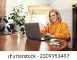 Happy mature woman using laptop while working remotely from home in living room