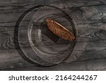 Small photo of Brown small piece of bread on large glass plate on black wooden table. Dark HDR photo. Simple food, meager food, poverty and malnutrition