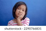 Small photo of Asian kid girl toothache. Kid suffering from toothache. Asian child hand on cheek face as suffering from facial pain, mumps toothache. Dental health care.