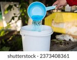 Small photo of In the garden a woman mixes a fertilizer solution in a bucket to feed the plants A woman prepares an aqueous solution of fertilizers to feed vegetables in the garden. Fertilizer concept in gardening.