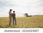 Small photo of Father and son watching combine harvester in field