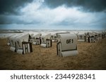 Small photo of Roofed wicker beach chairs at the baltic sea beach, coast at the island of Usedom in Germany, storm and rain over the brack water, high waves, storm warning