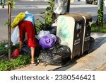 Small photo of Rear view of old scavenger woman collecting used good around the trash bin in the city road side