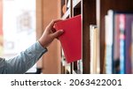 Small photo of Close up of asian man checking interesting book from bookcase to searching a book and taking off book from the bookshelf in library while reading a book to relaxation from work hard