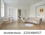 Small photo of Interior of light lounge with white walls and solid herringbone oak parquet with round table decorative lights on ceiling and oval beige sofa