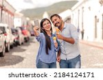 Small photo of A young couple of Hispanics walk through the streets of a colonial city with an artisanal ice cream in their hands. Young tourists are enjoying their vacations in a beautiful city.