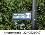 Public Restrooms sign on a black post in front of a green tree.