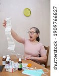 Small photo of Elderly amazed woman reading annotation to medicines at table at home