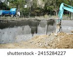 Small photo of Digger working on construction site against a rain waterd building Foundation - stock photo Excavation in rock strata for building foundation near Marseille France