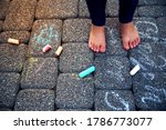 The child paints chalk on the path. Child draws patterns on asphalt. Square chalk of different sizes for drawing. Puffy legs of the baby and multicolored chalk
