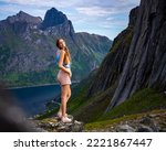 beautiful girl stands on the rocks above the precipice enjoying the view of the famous segla mountain in norway, senja island; hesten trail head, the famous norwegian fjords with mighty mountains