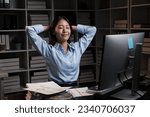 Young beautiful Asian business woman relaxing after working at her desk, working overtime at night.