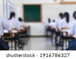 Small photo of Blurred of undergraduate students testing of examination in room and student sitting on row chair doing final exams in classroom with Thailand uniform. Asian Education Concept.