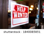 Sign text closeup for help wanted with red and white colors by entrance to store shop business building during corona virus covid 19 pandemic