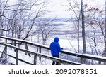View of man standing on wooden bridge looking down at frozen Missouri River floodplain on cold winter day in Midwest; Missouri River bluffs in background