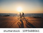 Couple of young hipsters cycling together at the beach at sunrise sky at wooden deck summer time