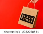 Female hand holding craft shopping bag with Black Friday text on red background. Sale, discount, shopping concept