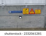 Blue, yellow, and red warning signs on a grey concrete wall with steel railing in Iceland